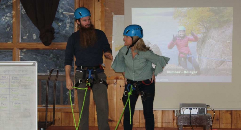 Two people stand inside, but in safety gear, in front of a screen displaying a presentation during the family seminar of an outward bound intercept course.